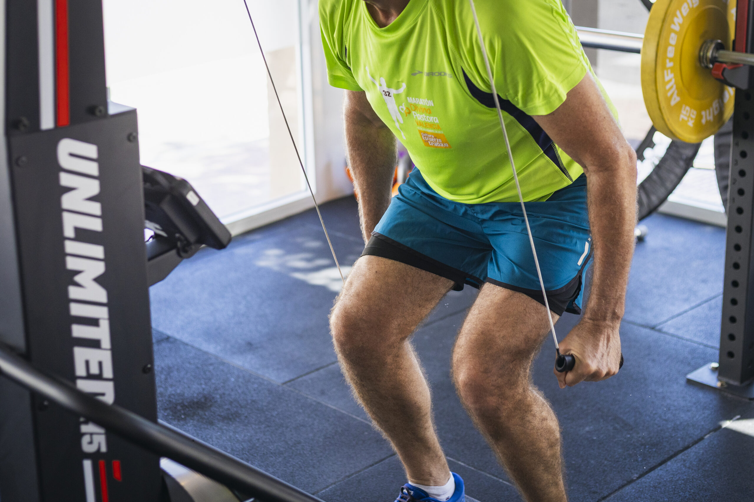 Persona realizando entrenamiento de resistencia y fuerza con una máquina de poleas o cable en un gimnasio. Ejercicio de tracción o jalón para fortalecer el core, la espalda y las piernas.