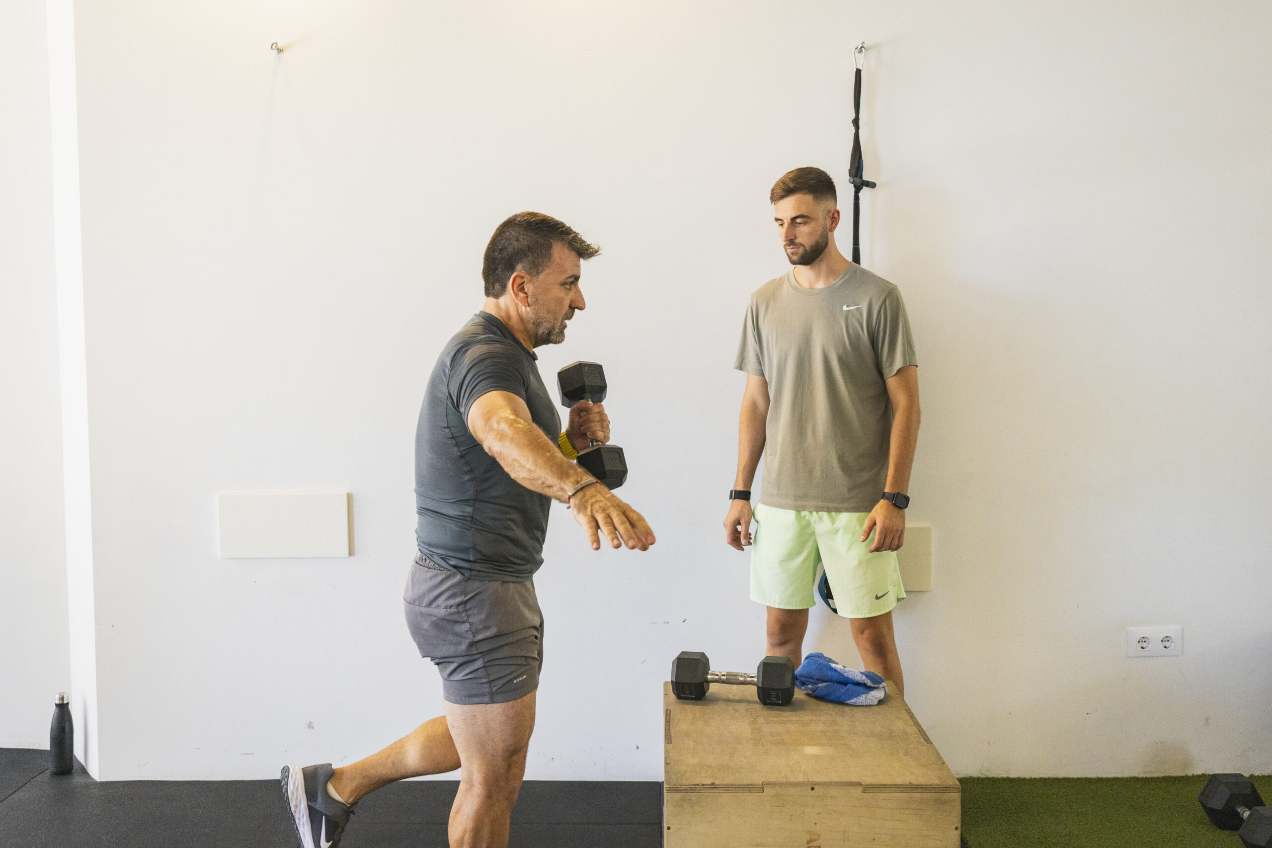 Entrenamiento personal en un gimnasio. Una persona realiza un ejercicio de peso muerto a una pierna con una mancuerna para mejorar el equilibrio y fortalecer el core y los glúteos, mientras es supervisada por un entrenador.
