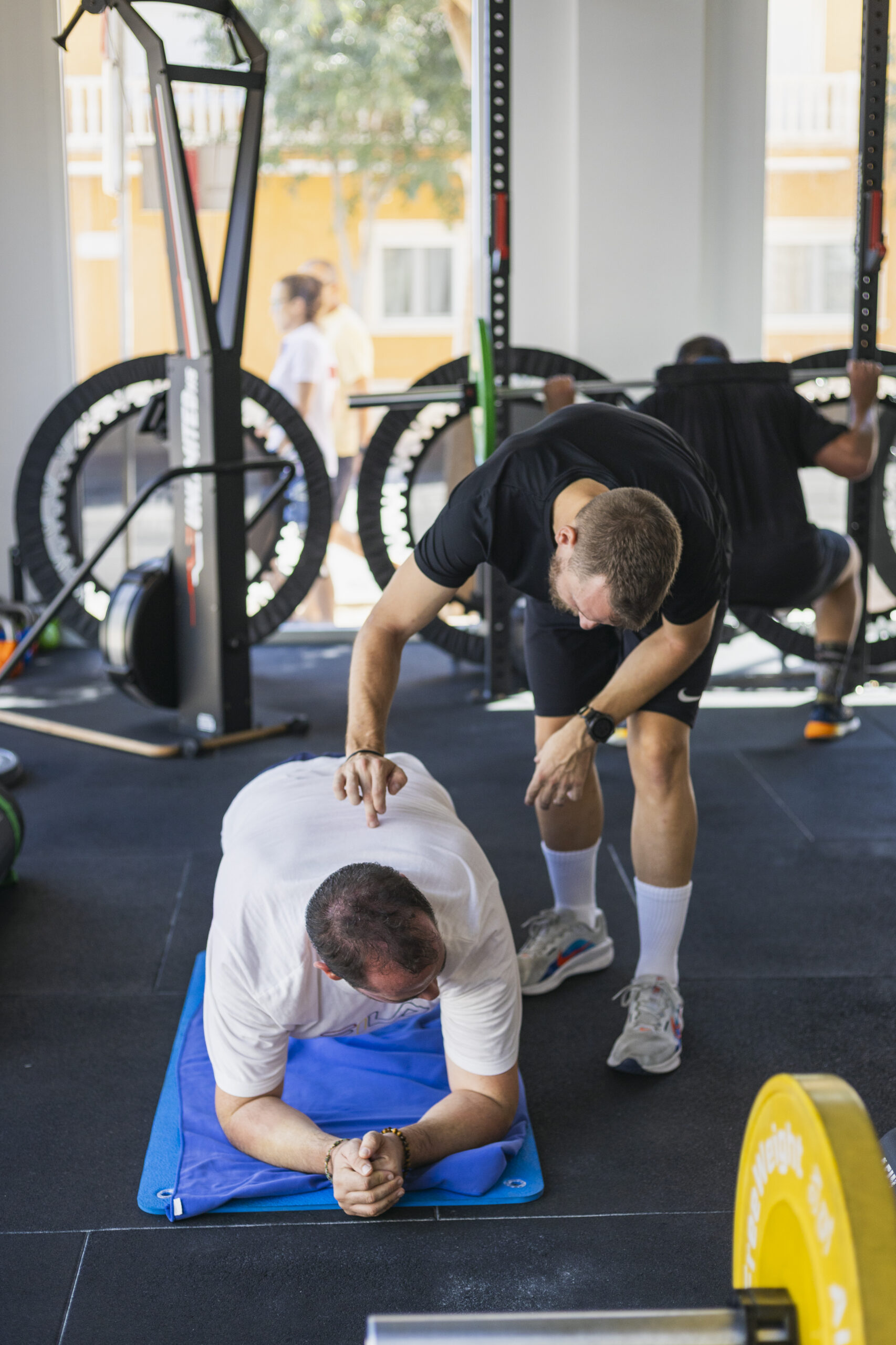 Entrenamiento del core o abdomen en un gimnasio. Una persona mantiene la posición de plancha (plank) sobre una colchoneta, recibiendo supervisión y corrección de postura por parte de un entrenador personal.